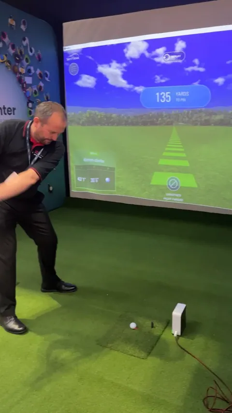 A golfer taking a shot in the ex-demo bay, with the simulator on the impact screen