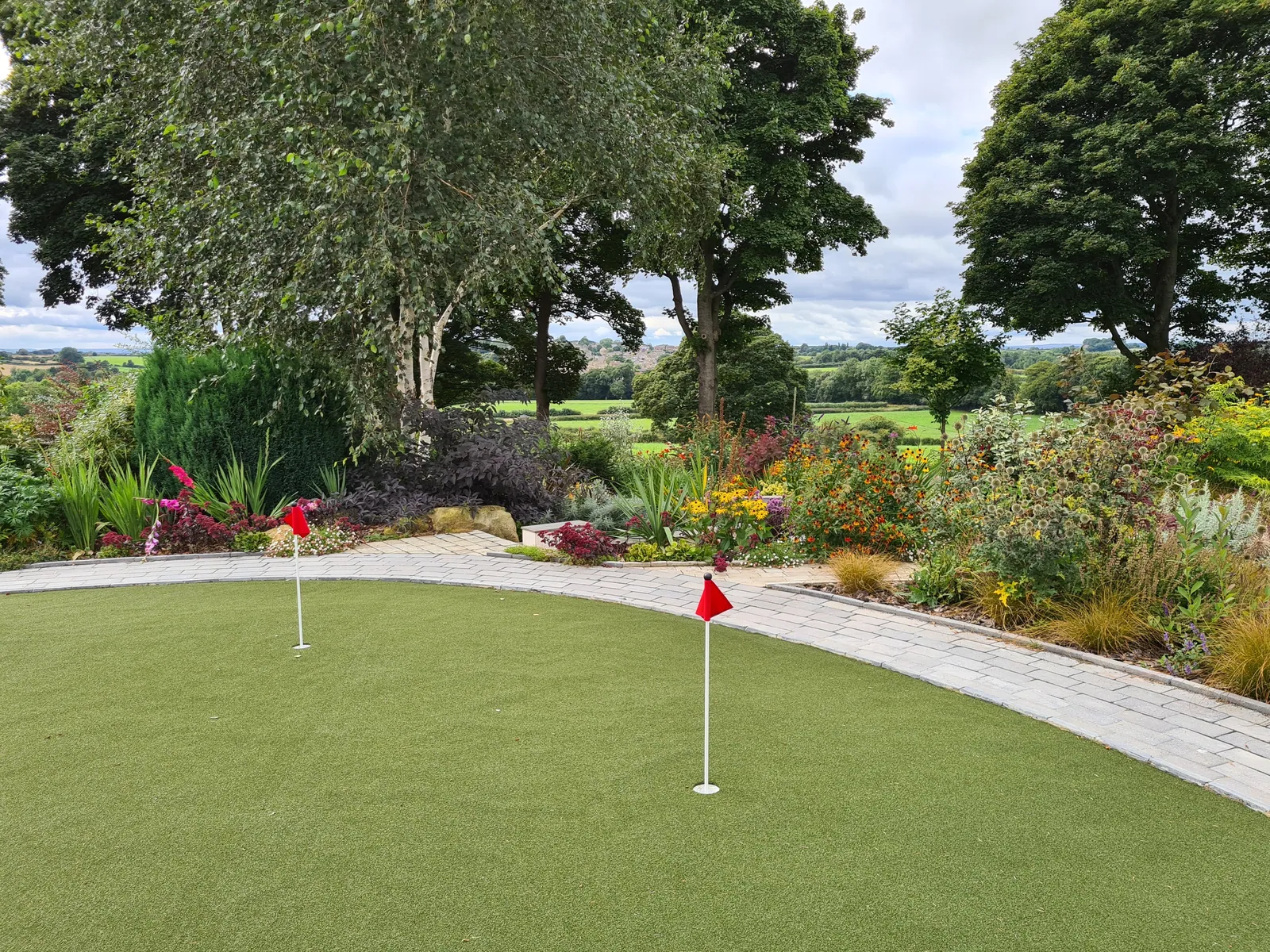 A garden putting green with red flags, a stone path and borders of planting