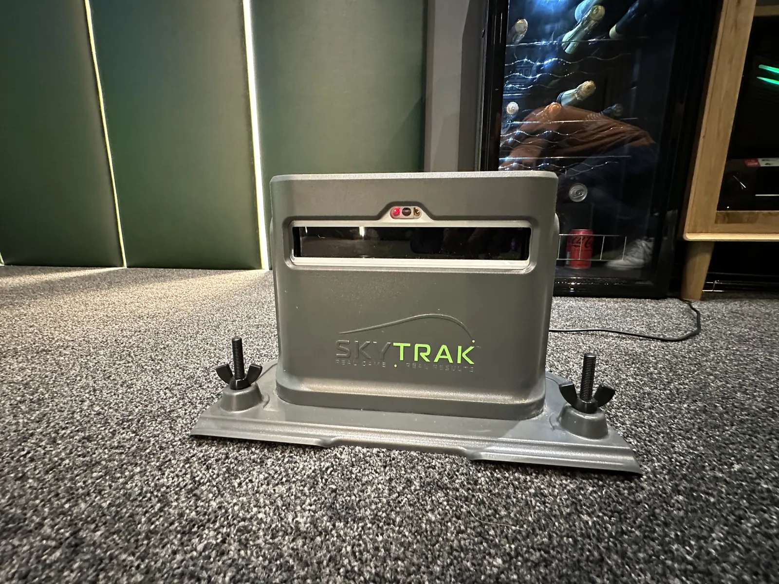A SkyTrak launch monitor on a floor mount in a simulator room