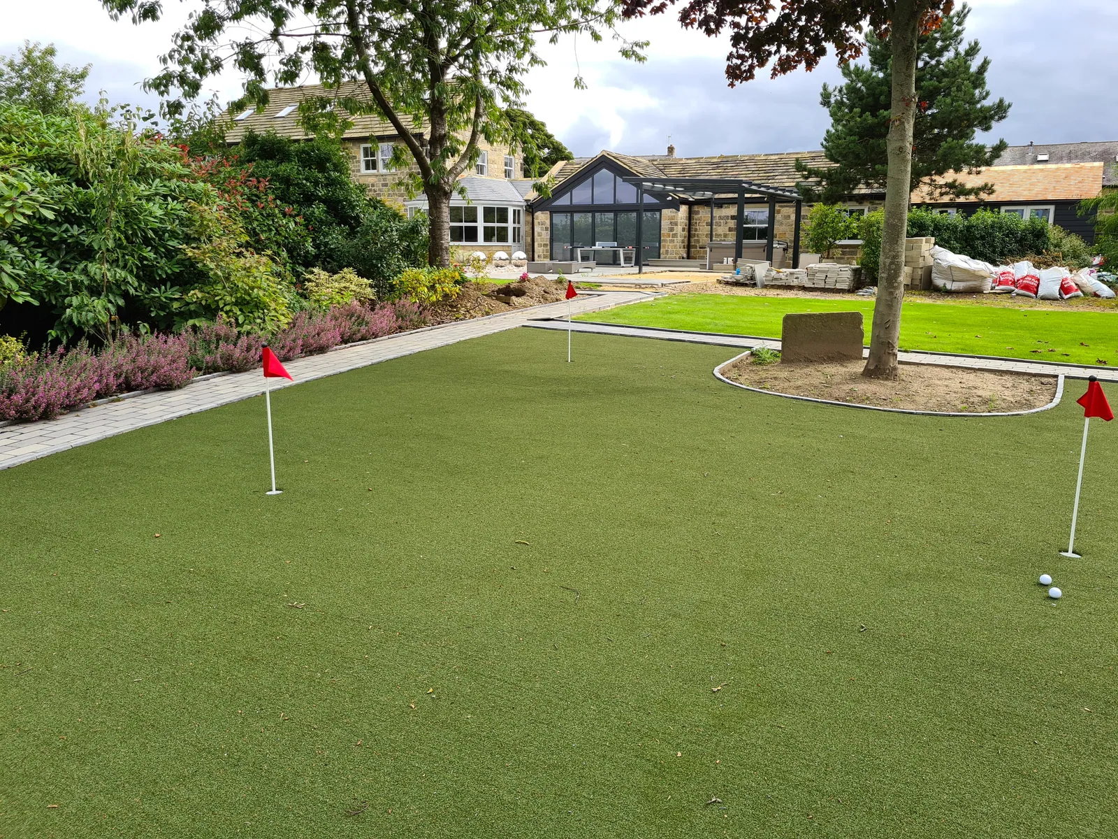A wide putting green with flags, golf balls and a country house behind