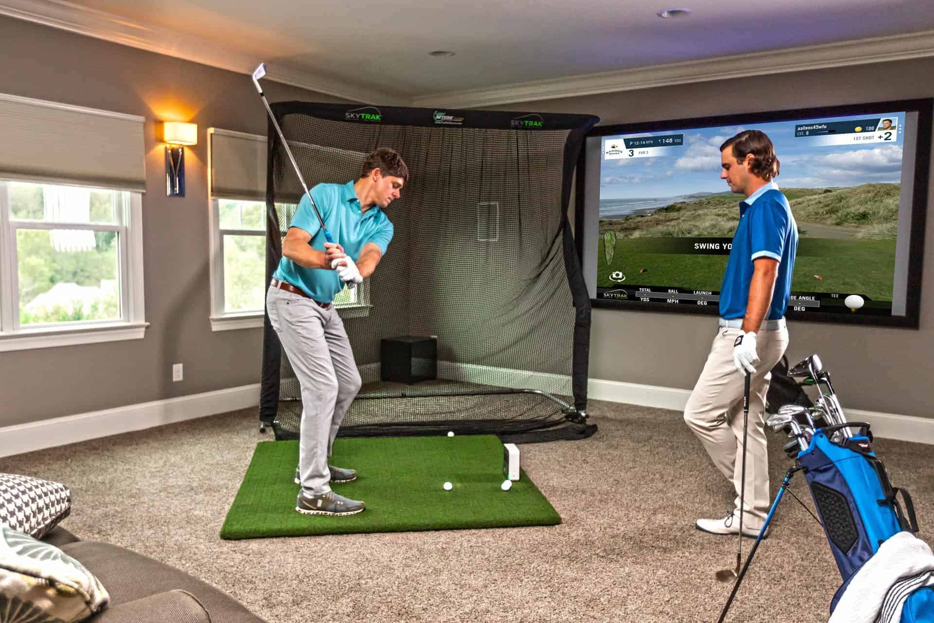 Two men practicing their golf swing using a SkyTrak living room golf simulator